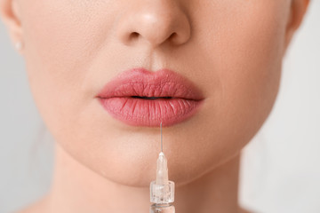 Young woman receiving filler injection against grey background, closeup