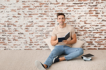 Fototapeta premium Handsome young man reading books near brick wall