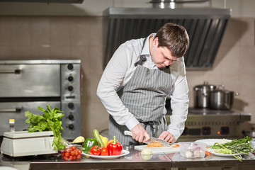 Young chef cutting beet on a white cutting board closeup. Cooking in a restaurant kitchen