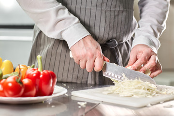 Closeup of hand with knife cutting fresh vegetable. Young chef cutting beet on a white cutting board closeup. Cooking in a restaurant kitchen
