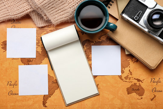 Empty notebook with paper sheets, photo camera and cup of tea on world map