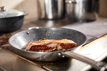 fried ribs of lamb. Cooking with fire in frying pan. Professional chef in a kitchen of restaurant cooking. Man frying food in flaming pan on hob.