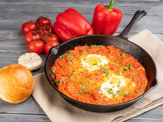 Shakshuka with bell pepper, tomatoes, hummus and rolls.