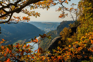 View over the Elbe valley in Saxon Switzerland on a sunny autumn day. Rocks and river Elbe with trees and village in the background with blue sky with clouds