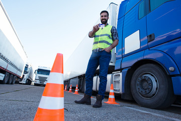 Portrait of middle aged bearded truck driver standing by his truck and showing his commercial...