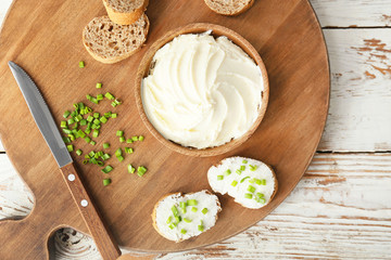 Fresh bread with tasty cream cheese and green onions on table