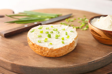 Fresh bun with tasty cream cheese and green onions on wooden board, closeup