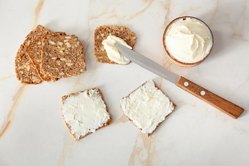 Fresh bread and tasty cream cheese with knife on table