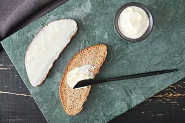 Fresh bread and tasty cream cheese with knife on table
