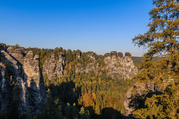 Panoramic view of the rocks of the Elbe Sandstone Mountains. Sunny day with autumn mood in Saxon Switzerland. Coniferous and deciduous trees with blue sky