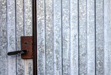 Grey metal gates with a pattern in the form of vertical strips are closed on a rusty lock with an old handle, on which the paint was covered