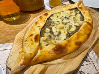 Khachapuri with meat and cheese on a wooden board. A dish of Georgian cuisine. Close-up