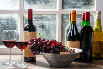 two wineglasses, red and white grapes with bottles of red wine