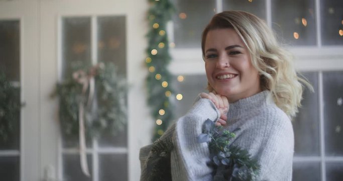 Woman in warm sweater laughs with christmas wreath in her hands, decorating the scandinavian interior for christmas, cozy new year's home atmosphere, 4k DCI 120fps Prores HQ