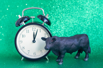 bull as a symbol of the new year 2021 on a green shiny background next to an alarm clock and a branch of the Christmas tree