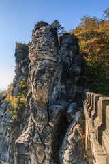Fototapeta na wymiar Lateral view of the Bastei bridge in Saxon Switzerland. Rocks and trees in autumn mood with a terrace view of the Elbe Sandstone Mountains with blue sky and sunshine