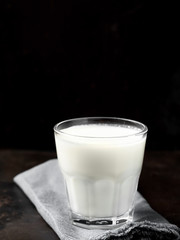A glass with fresh milk or yogurt on a blue stand is located on a dark metal background. Close-up. Vertical orientation, space for text. Shallow depth of field.