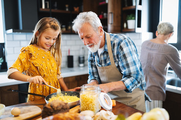 Smiling grandfather helping children to cook in the kitchen