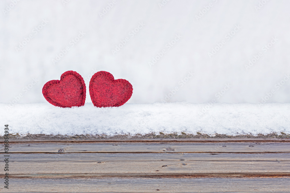 Wall mural two red hearts of red fur on white snow and a wooden background. love and valentines day concept.