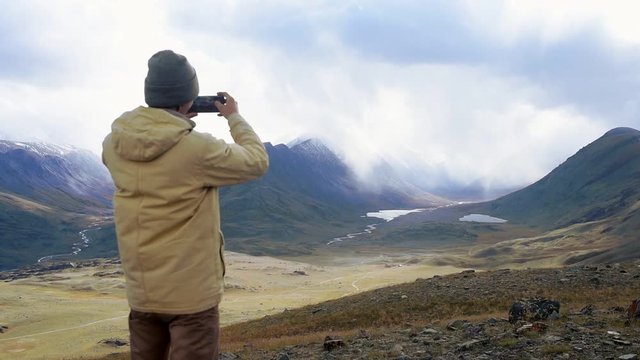 Hiker photographer takes pictures of mountains with smartphone with lake view. Epic view of the valley with a river, Altai