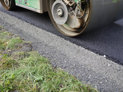 Planierwalze walzt frischen Asphalt am Fahrbahnrand