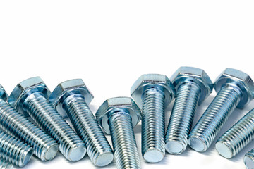 Metal industrial bolts with threads are laid out on the edge on an isolated light background. Selective focus, copy space.