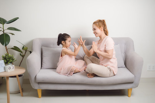 Happy young woman playing clapping game with female child while sitting in livingroom