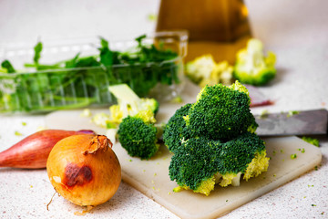 Onions, broccoli florets, knife and oil on kitchen board.