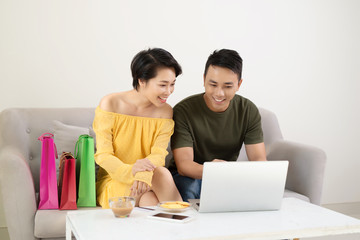Fototapeta premium Happy young Asian couple watching online stores using laptop to purchase at home.