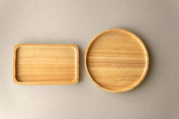 Top view empty above round wooden plate next to square tray on grey organic paper background.