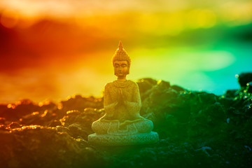 Figure of a buddha meditating by the sea at sunrise