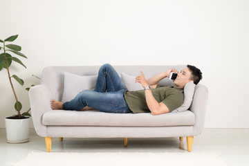 Relaxed man using a smart phone lying on an couch/sofa in the living room at home
