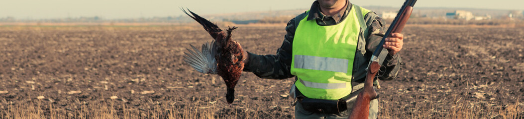 A man with a gun in his hands and an orange vest on a pheasant hunt in a wooded area in cloudy...
