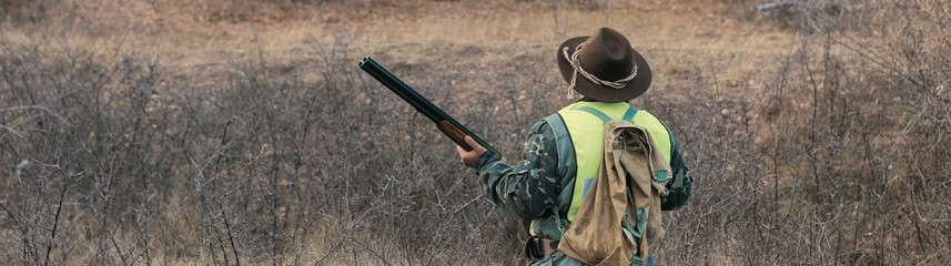 A man with a gun in his hands and an green vest on a pheasant hunt in a wooded area in cloudy...