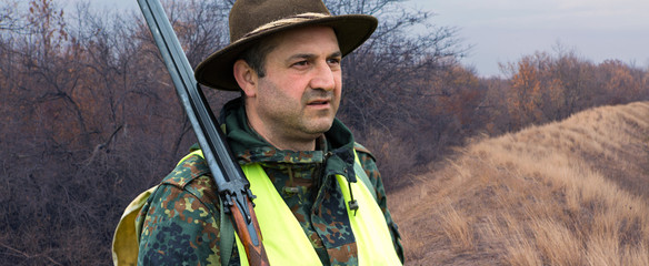 A man with a gun in his hands and an green vest on a pheasant hunt in a wooded area in cloudy...
