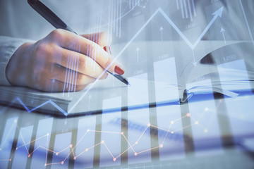 Multi exposure of woman's hands making notes with forex graph hologram. Concept stock market analysis.