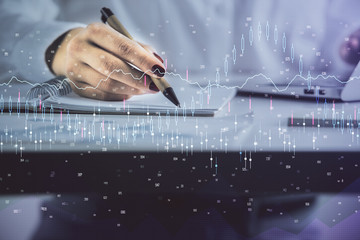 Double exposure of woman's hands making notes with forex graph hologram. Concept technical analysis.