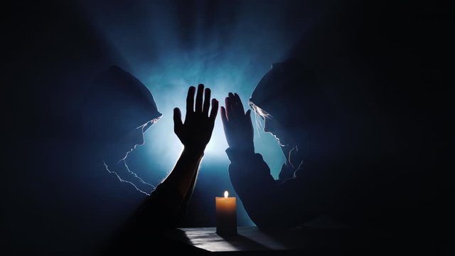 Two men in hoodies pray in the dark in the rays of light