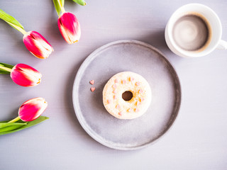 Kaffeepause mit einem Donat, einer Tassee Kaffee und frischen Tulpen, Frühling