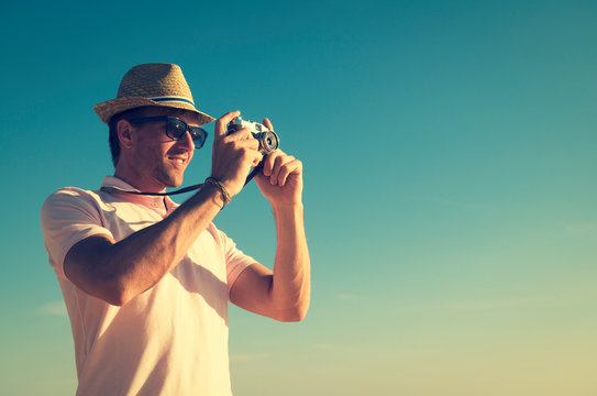 Retro tourist photographer with hat and sunglasses taking a photo with an old fashioned point and shoot camera