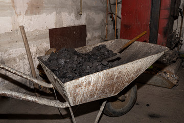 Wheelbarrow loaded with coal standing in the boiler room next to the furnace and firewood.