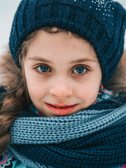 A girl in a winter jacket, hat and pigtails walks in the winter on the street, blush from the frost, winter entertainment