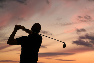 Golfer swinging a golf club silhouetted against a dusk sky