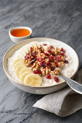 Healthy cereal breakfast, oatmeal topped with banana slices, dried cranberries, walnut, served with honey