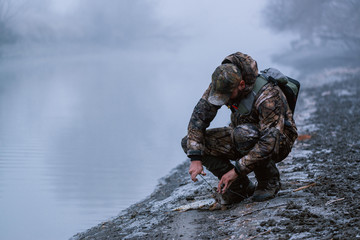 Naklejka premium Fisher man fishing with spinning rod on a river bank at misty foggy winter, spin fishing, prey fishing