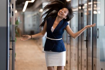 Fototapeta na wymiar Overjoyed Asian female employee dancing in office hallway