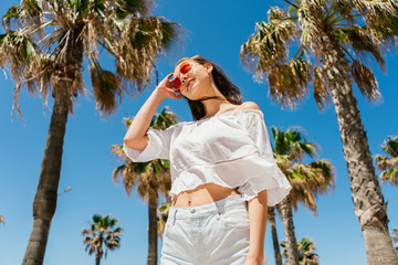 girl stands against the sky and palm trees touching her hands with glasses