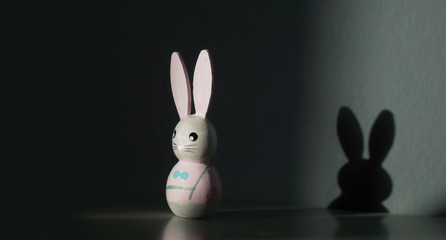Obraz premium easter bunny is standing next to the wall. shadow on the wall. Conceptual image with shadow of cute easter rabbit on the wall. shadow concept on happy easter decoration background.