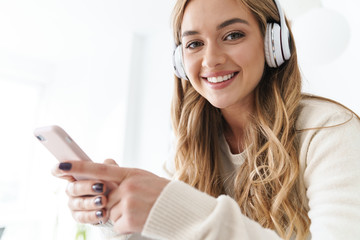 Photo of young smiling woman using headphones and cellphone