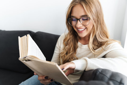 Photo of young smiling woman reading book while sitting on couch
